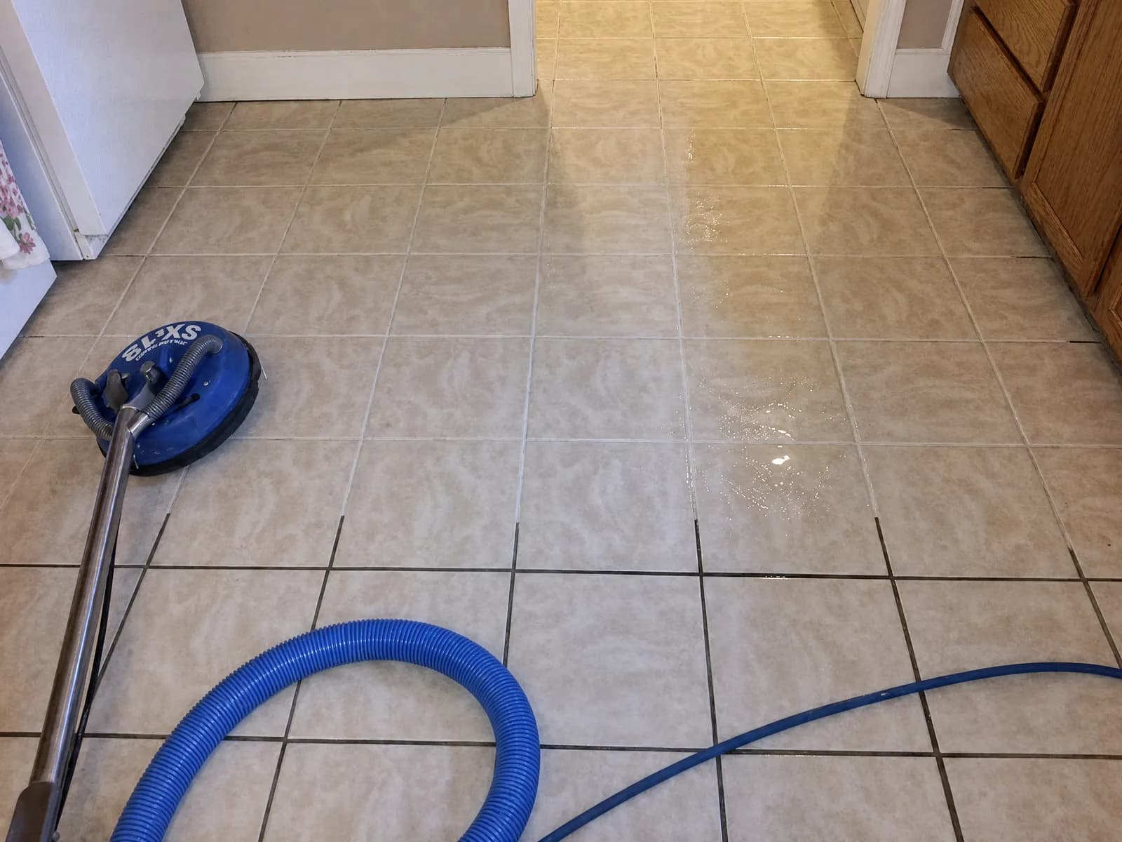 Tile-and-grout cleaning tool and hose on a beige ceramic floor, part-way through a clean
